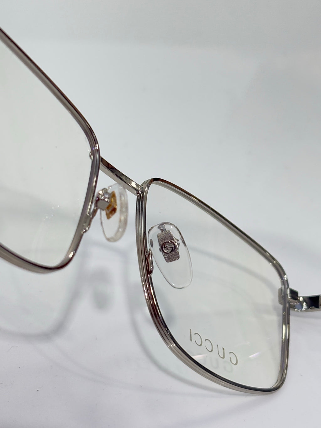 Eyeglasses close-up with silver metal oval frame and small logo emblem at hinge
