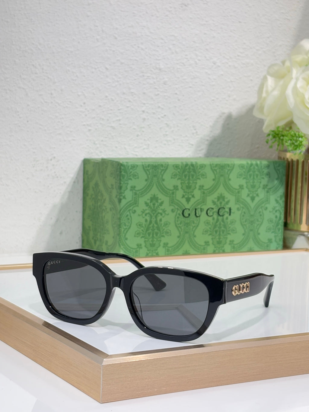 Gucci sunglasses with black frames and gray tinted lenses; squared, slightly rounded shape.