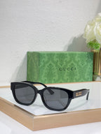Gucci sunglasses with black frames and gray tinted lenses; squared, slightly rounded shape.