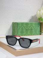 Gucci sunglasses with black frames, dark lenses; red and green temple accents.