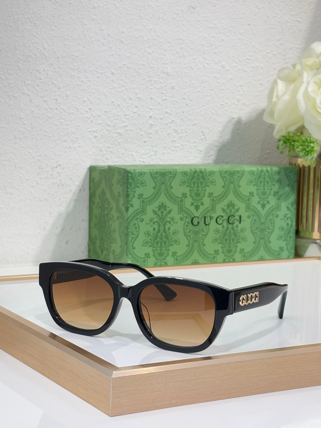 Gucci sunglasses with black frames and amber tinted lenses; squared cat-eye style.