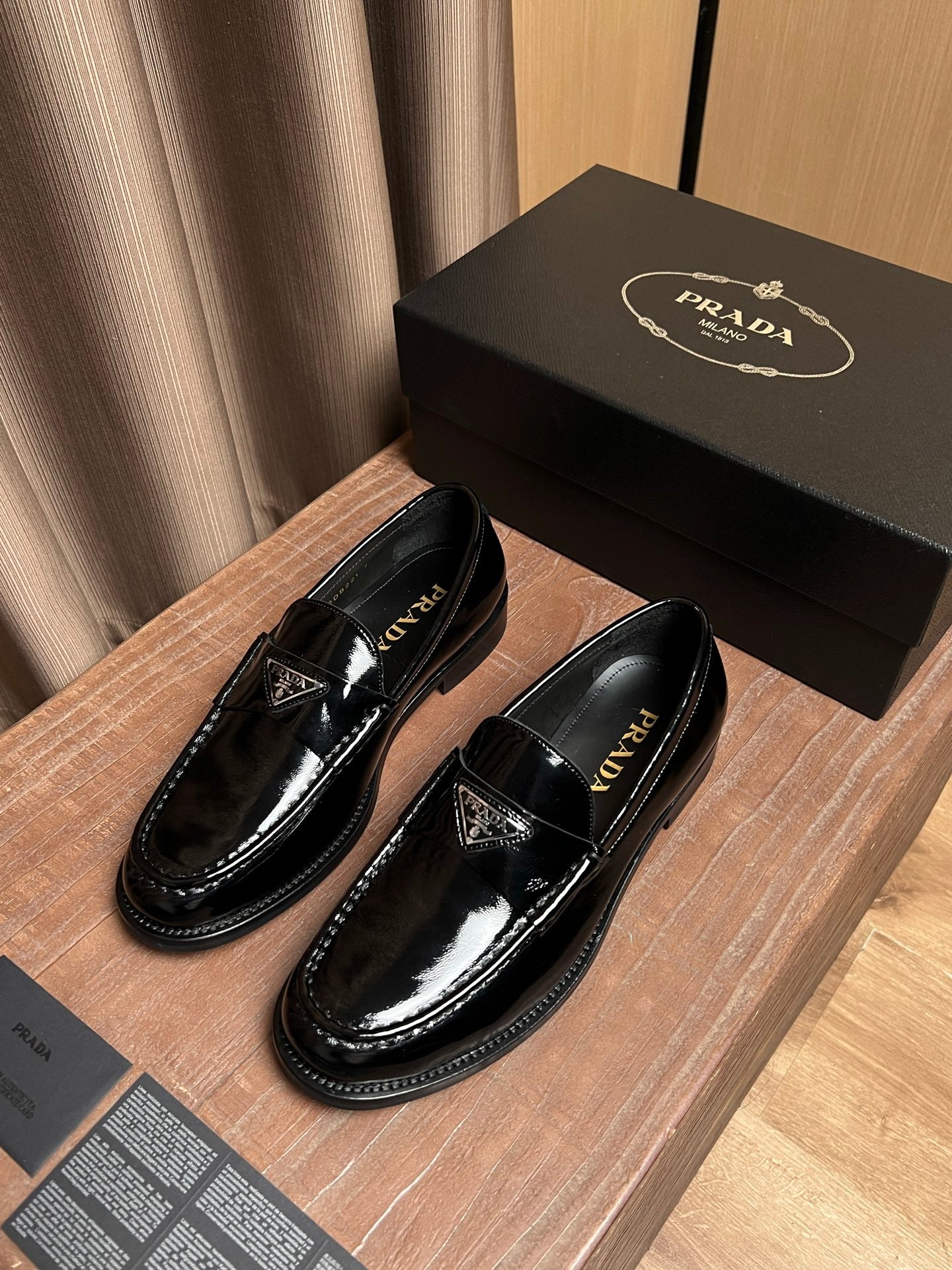 Black patent leather loafers with decorative triangular emblem on the vamp
