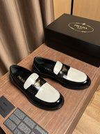 Black and white Prada loafers with gold triangle emblem, side view