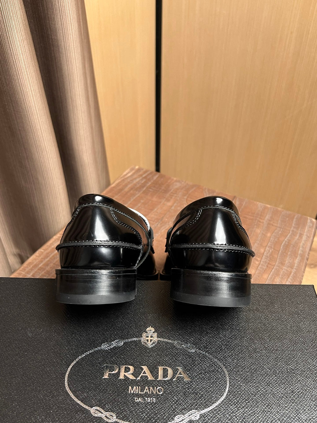 Prada loafers heel view: black leather with metal emblem and stitched edges