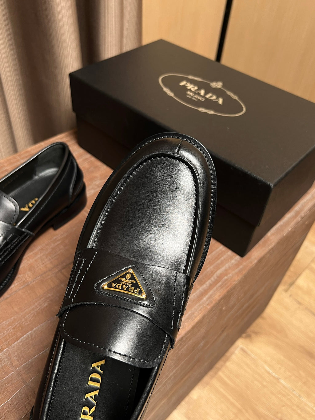 Black leather Prada loafer toe with raised gold triangle emblem and stitched edge