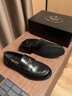Black leather Prada loafers with gold triangle emblem and slip-on loafer silhouette