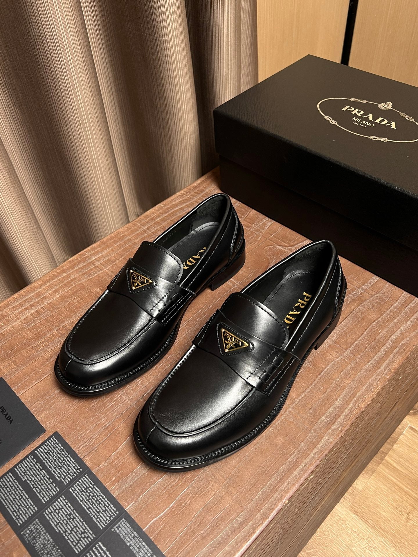 Black leather Prada loafers side view with decorative gold emblem and stitching