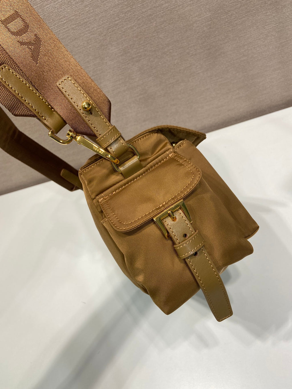 Prada tan bag with front buckle straps, flap pocket, and gold-tone metal accents