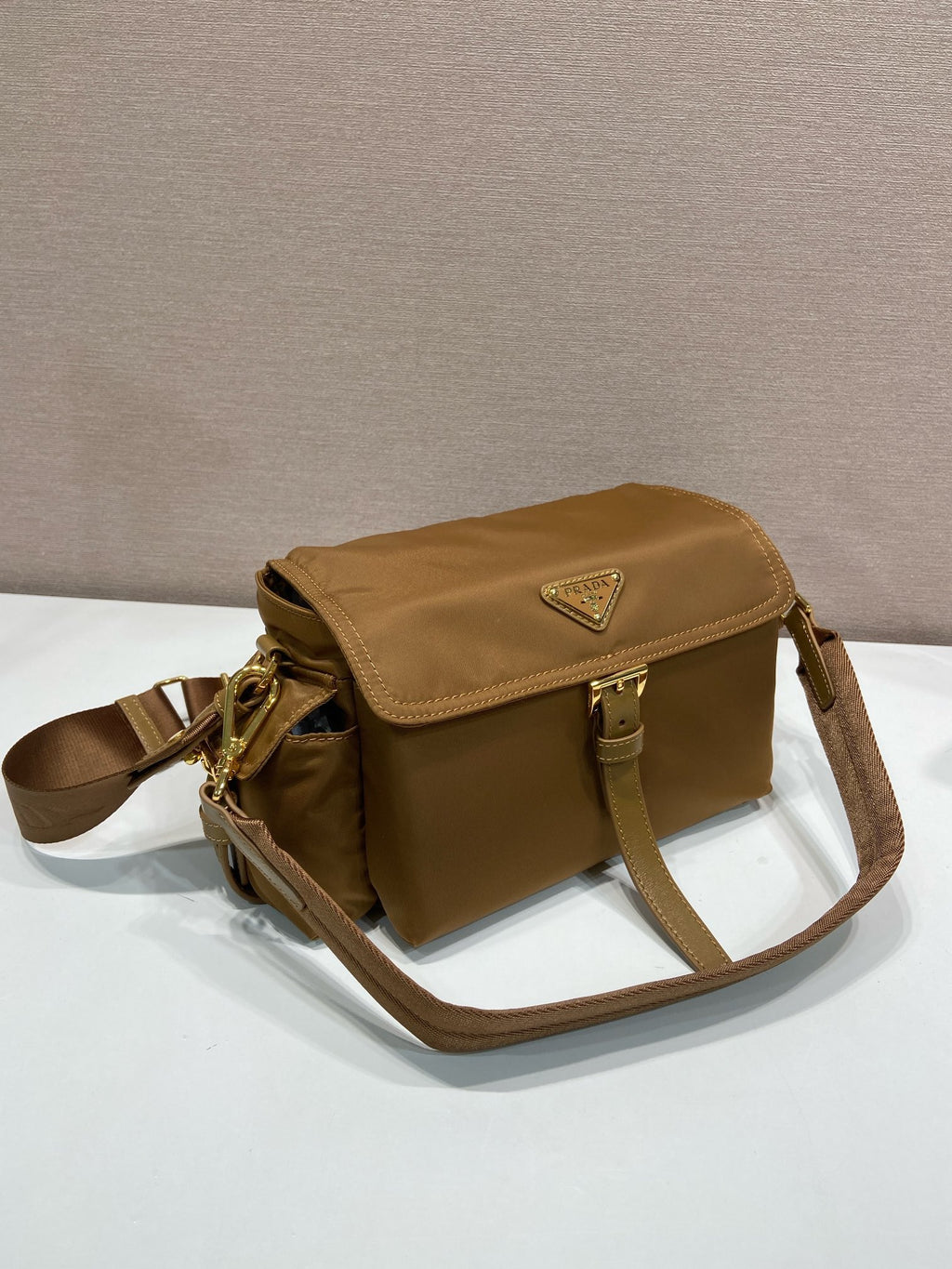Prada crossbody bag in tan with flap top, side straps, and gold hardware