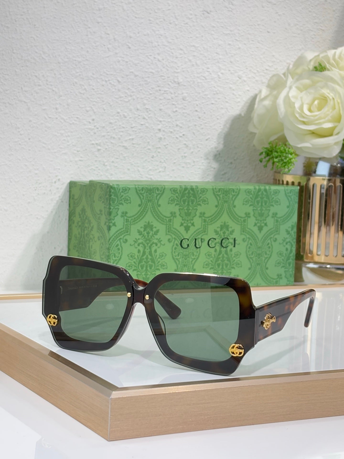Square sunglasses with dark brown frame and green-tinted lenses, gold logo detail