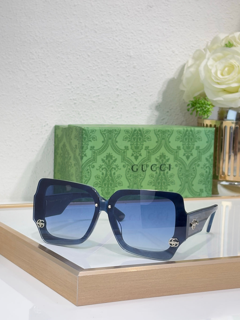 Square sunglasses with dark blue frame and blue-tinted lenses, gold logo detail