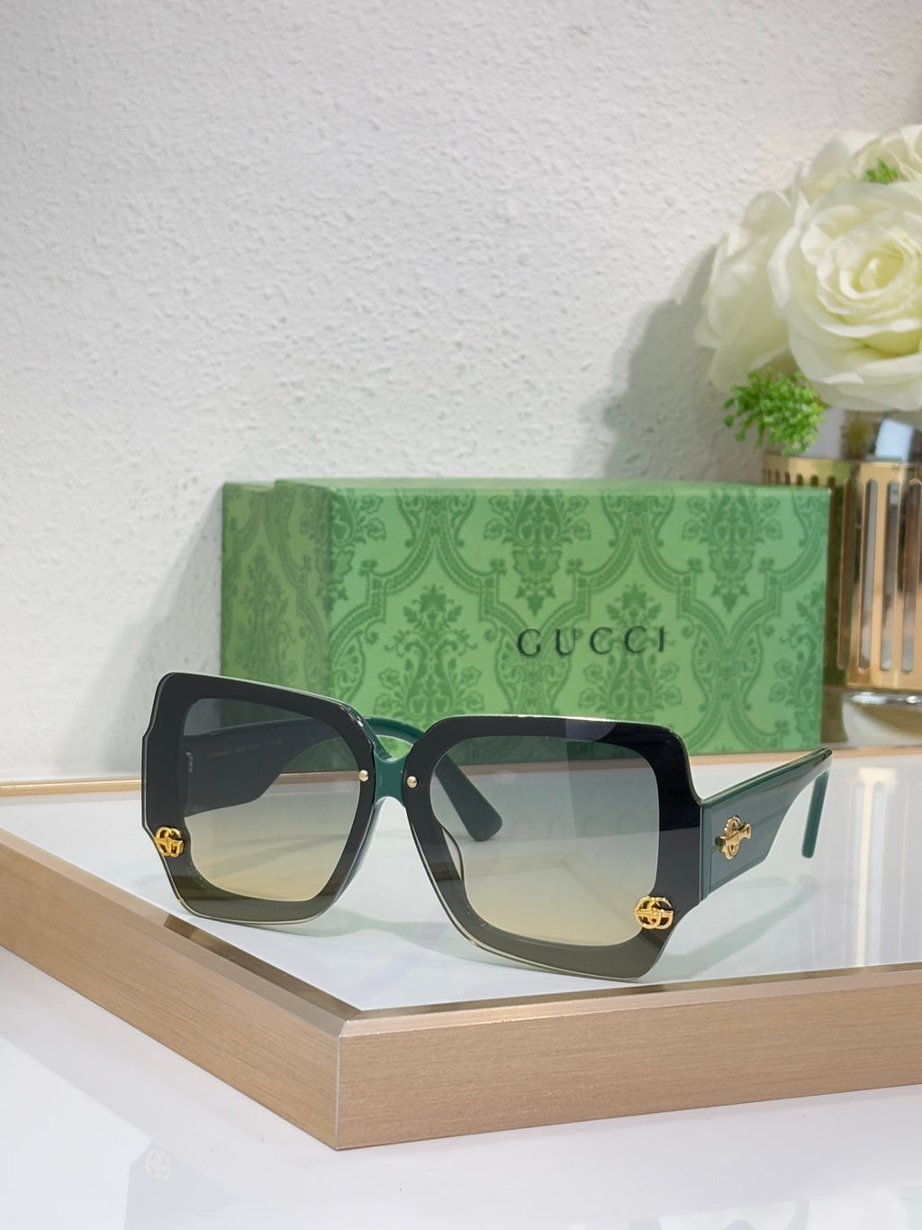 Square sunglasses with black frame and green-tinted lenses, gold logo detail