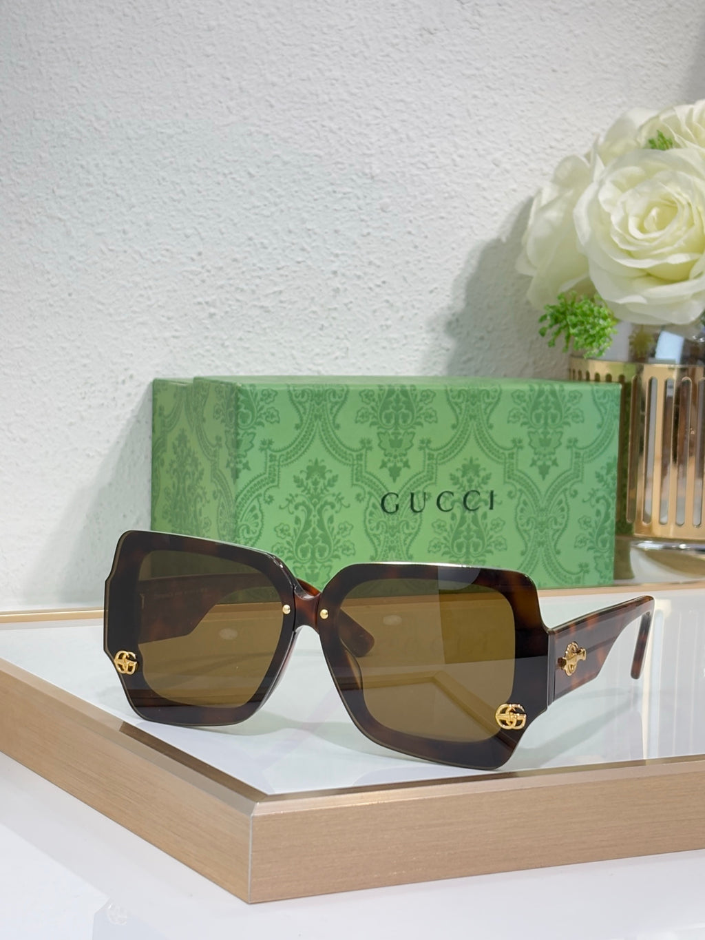 Square sunglasses with dark brown frame and dark amber-tinted lenses, gold logo detail