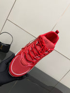 Red lace-up sneaker held in hand with raised tongue and textured upper