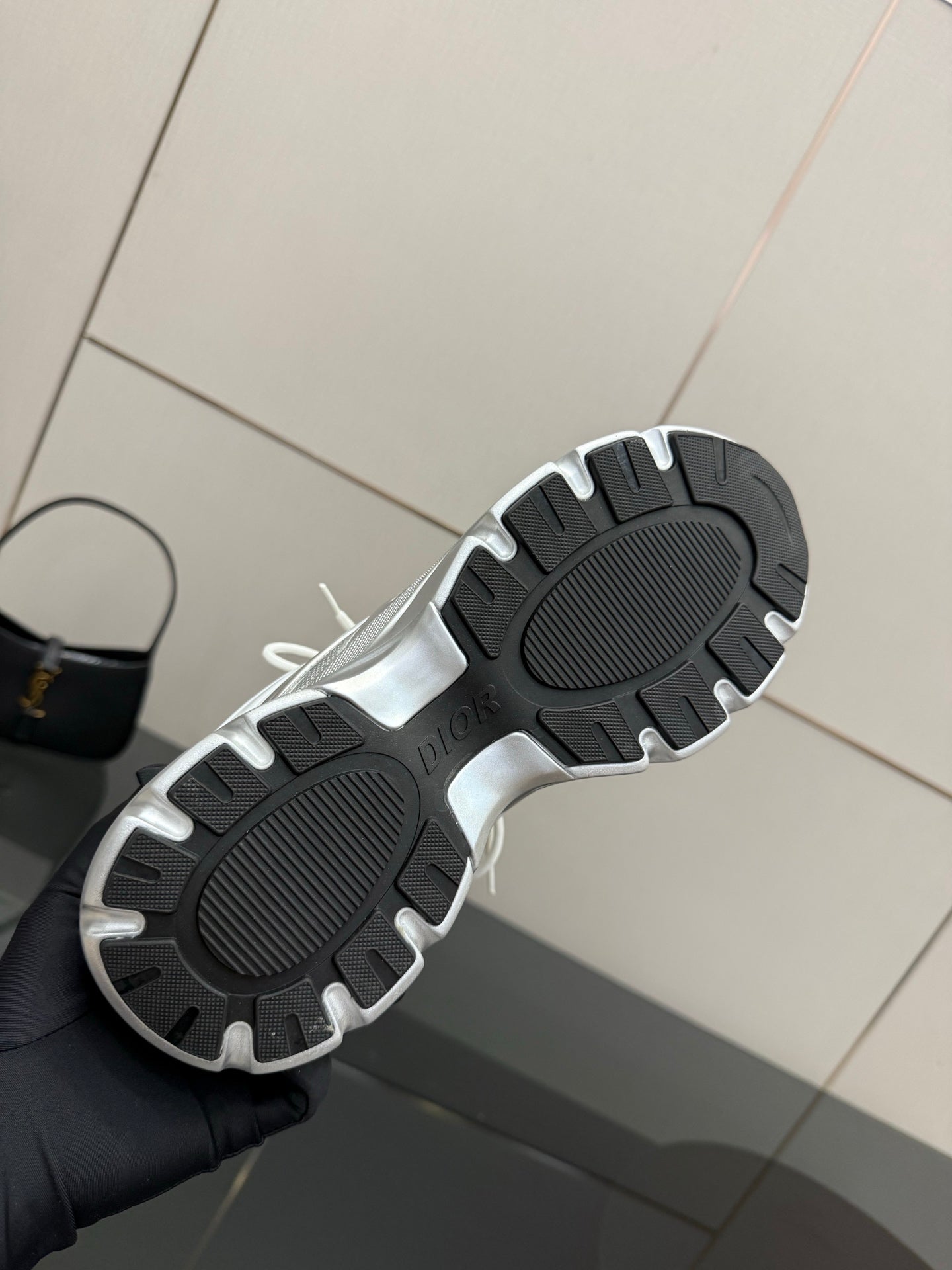 Outsole view of white low-top sneakers with black tread and Dior logo near heel