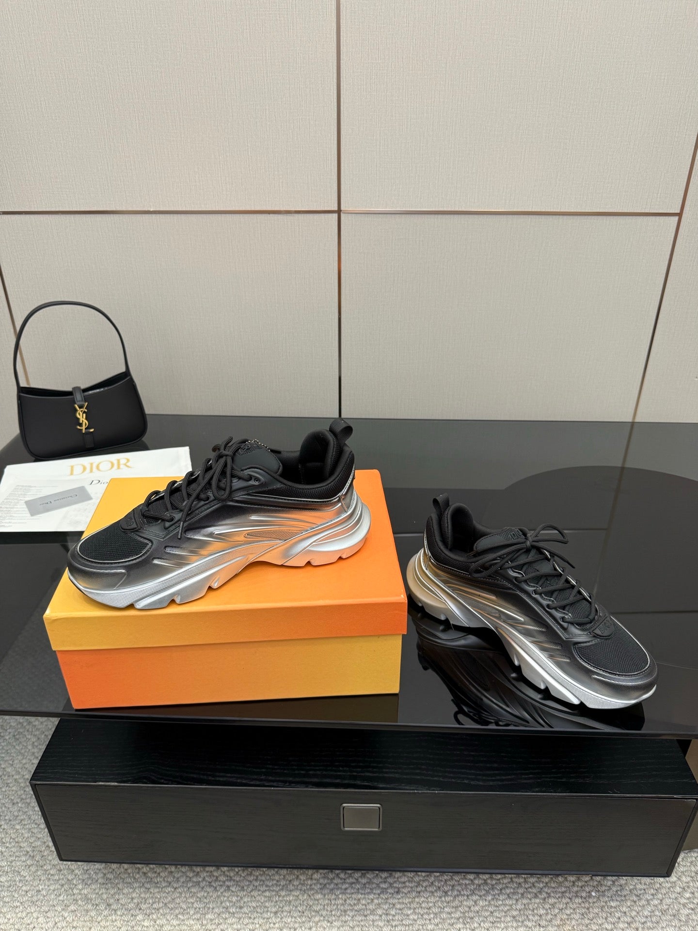 Two ladies' Dior sneakers on display, black uppers with silver soles and laces