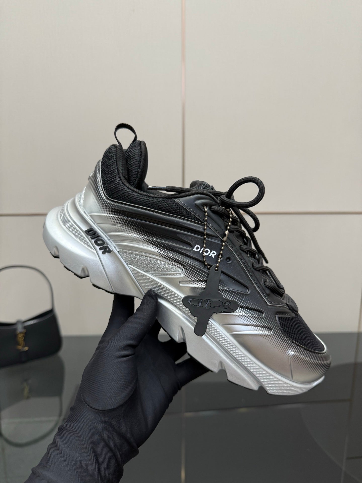 Ladies' Dior sneaker held up, black and silver colorblocked design with laces