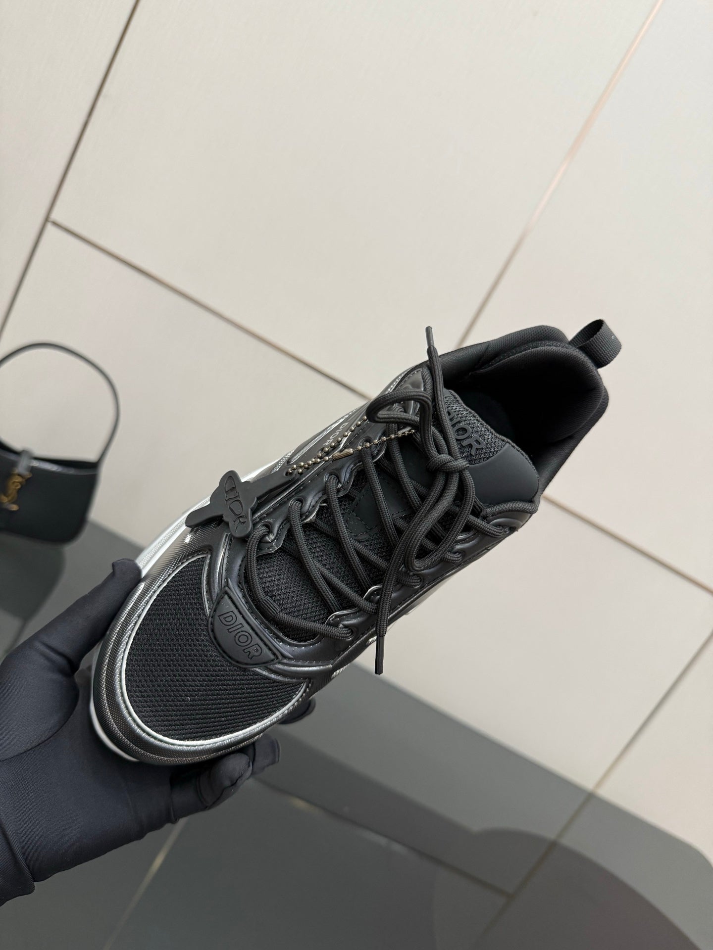 Ladies' Dior sneaker held by hand, black mesh upper with silver trim and laces