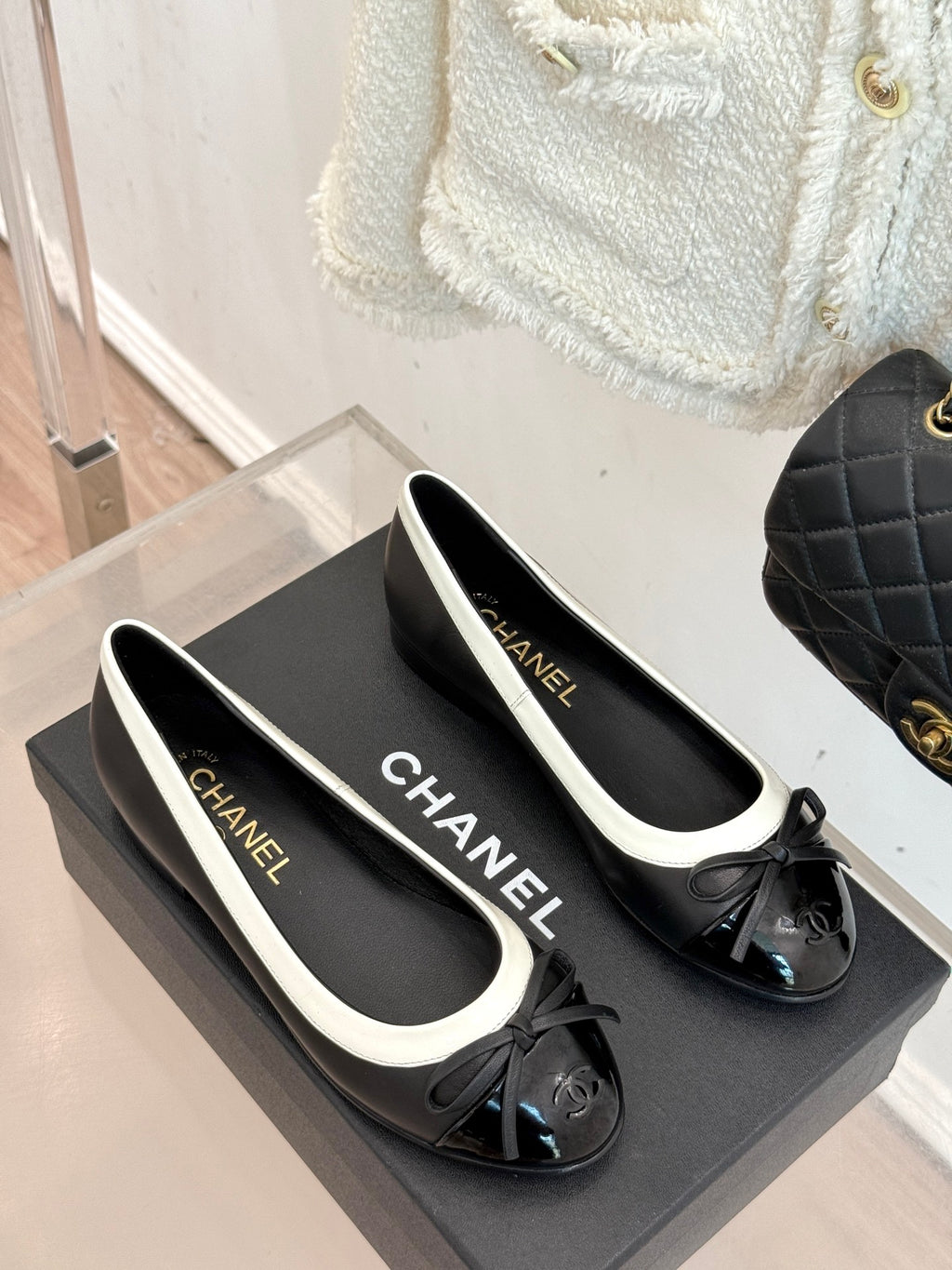Pair of black ballet flats with white piping, bows, and Chanel logo on insoles