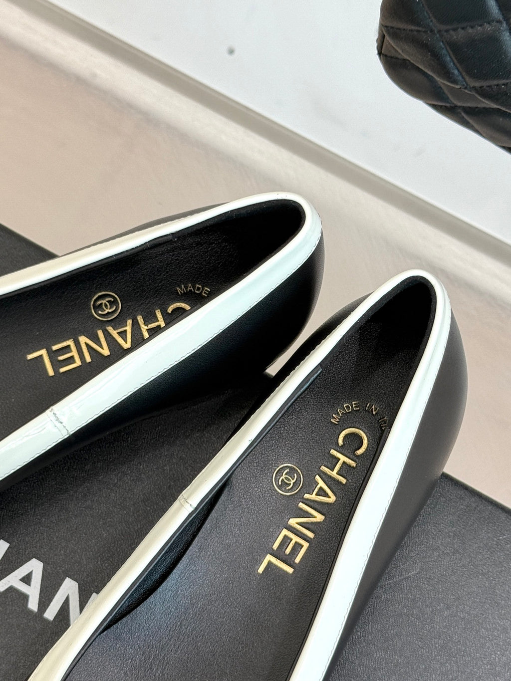 Black ballet flats with white trim and Chanel script on insole, angled view