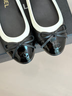 Close-up of black ballet flats with white trim and black bows, round toe