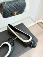 Black ballet flats with white edging and bow, shown on a shoebox