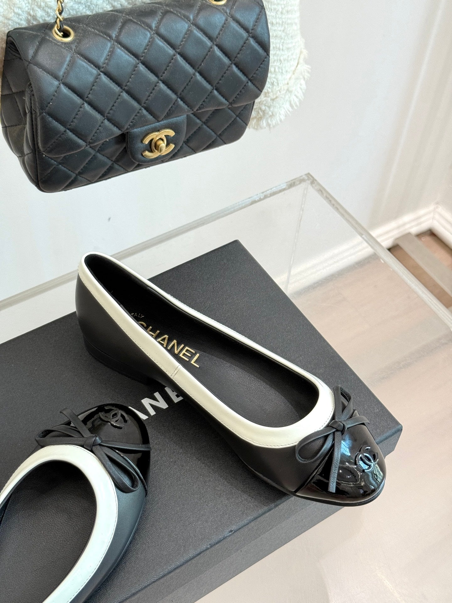 Black ballet flats with white edging and bow, shown on a shoebox