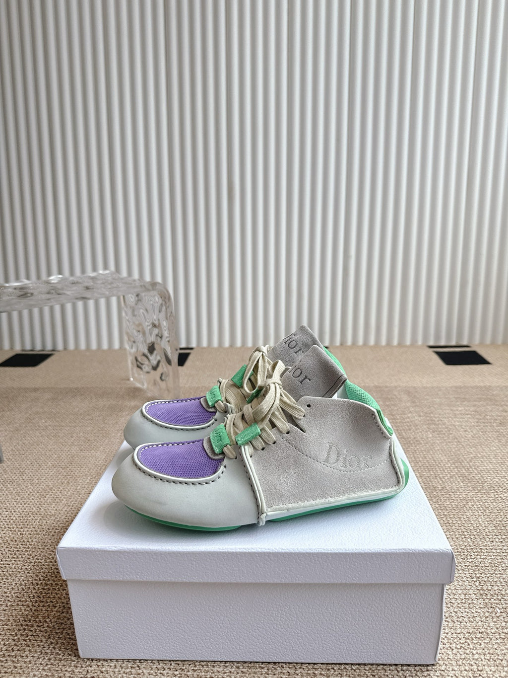 Front side view of sneakers: light upper, purple trim, and green lace details on box.