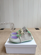 Front side view of sneakers: light upper, purple trim, and green lace details on box.
