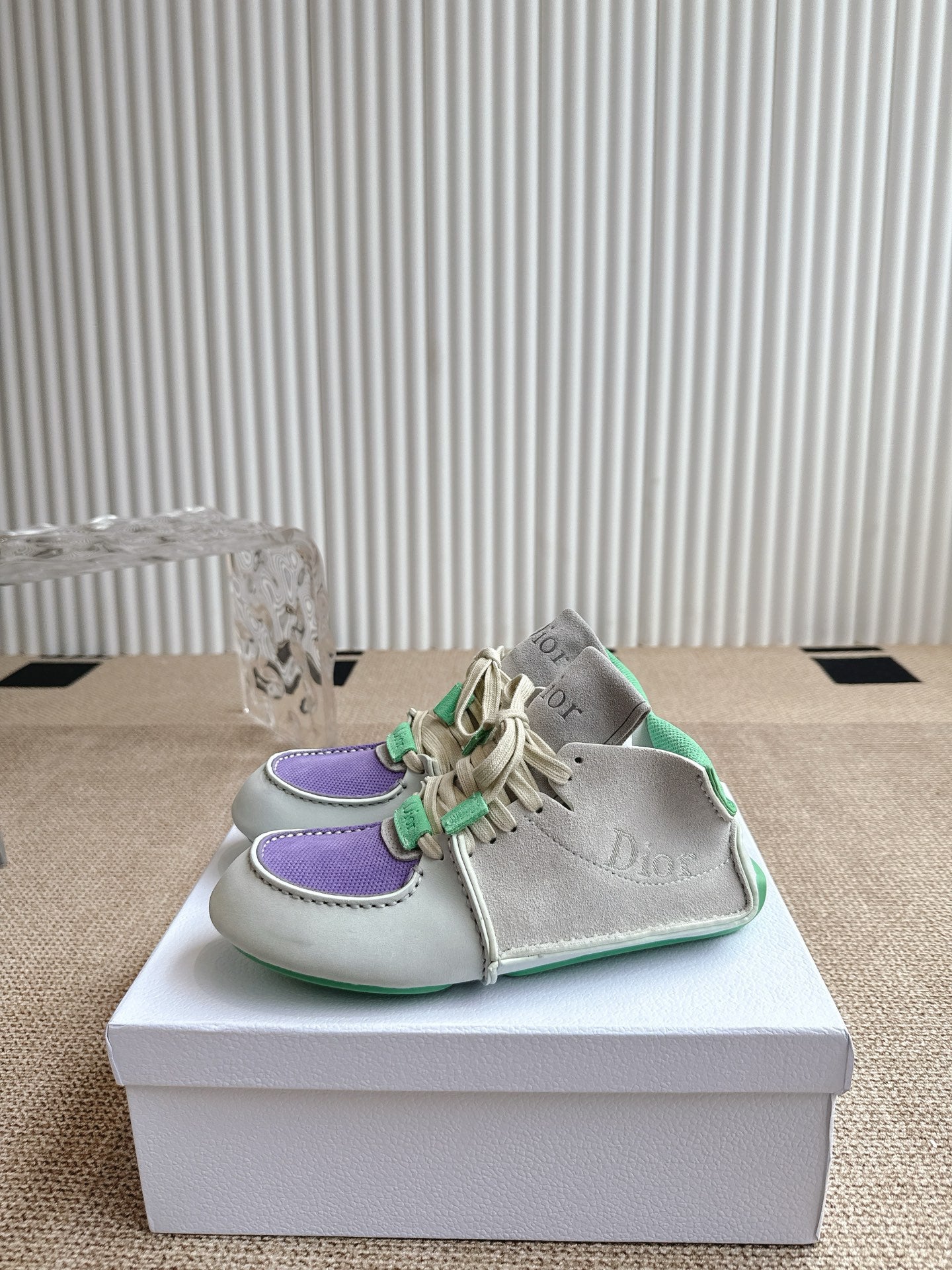 Front side view of sneakers: light upper, purple trim, and green lace details on box.