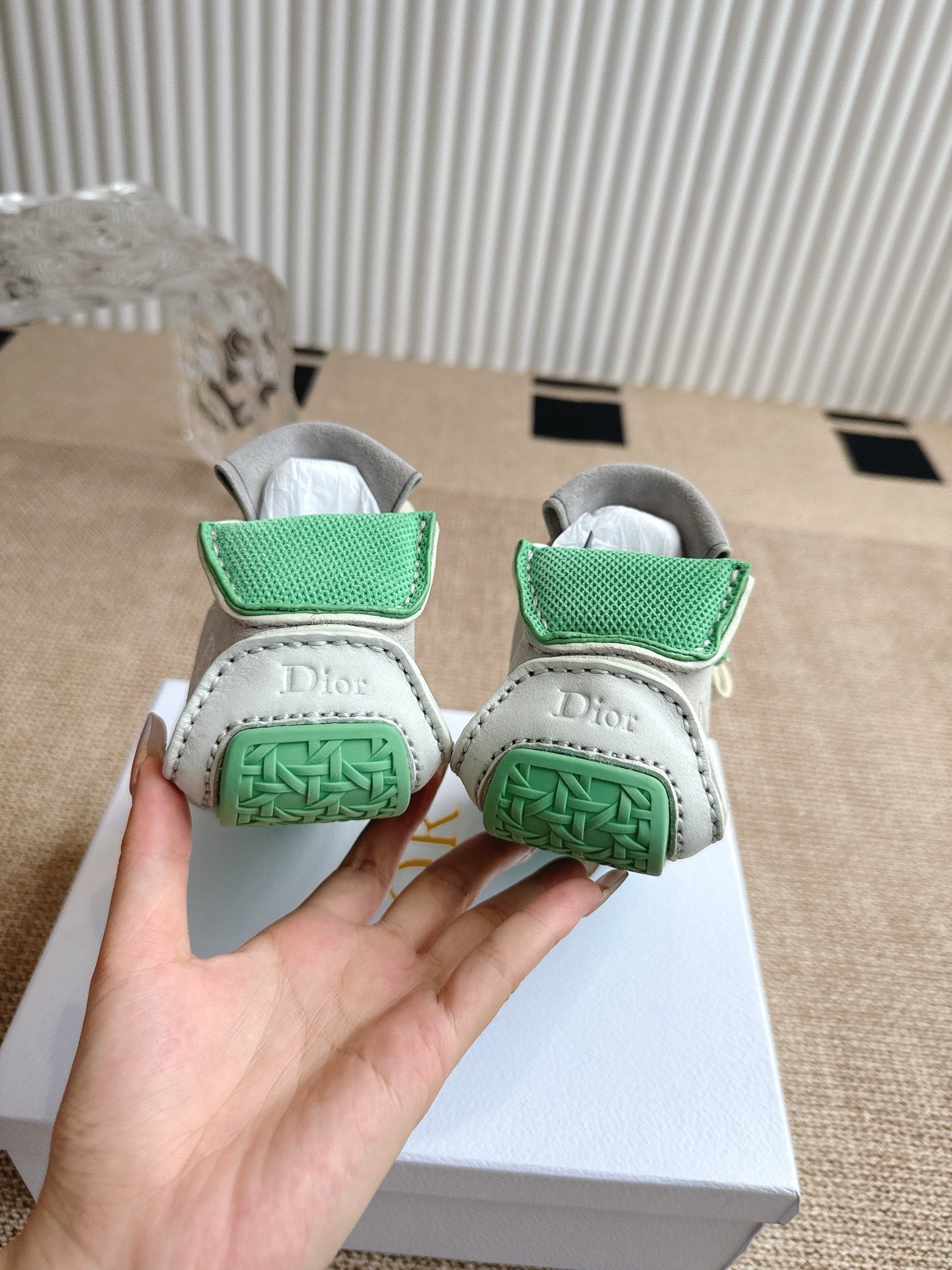 Back view of sneakers on box: light uppers with green woven heel straps.