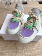Front view of low-top Dior sneakers with purple toe panel and green lace tabs on box.