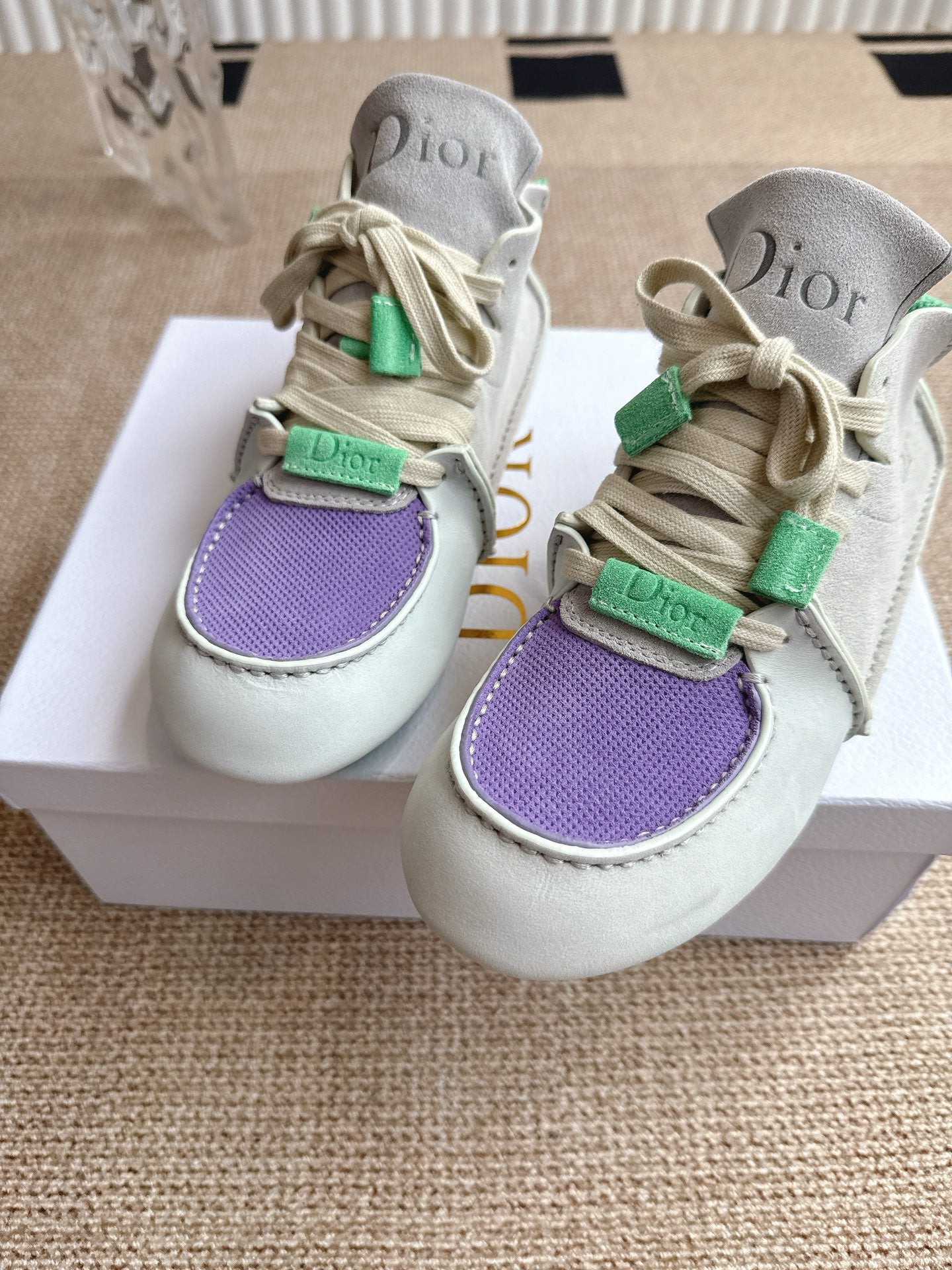 Front view of low-top Dior sneakers with purple toe panel and green lace tabs on box.