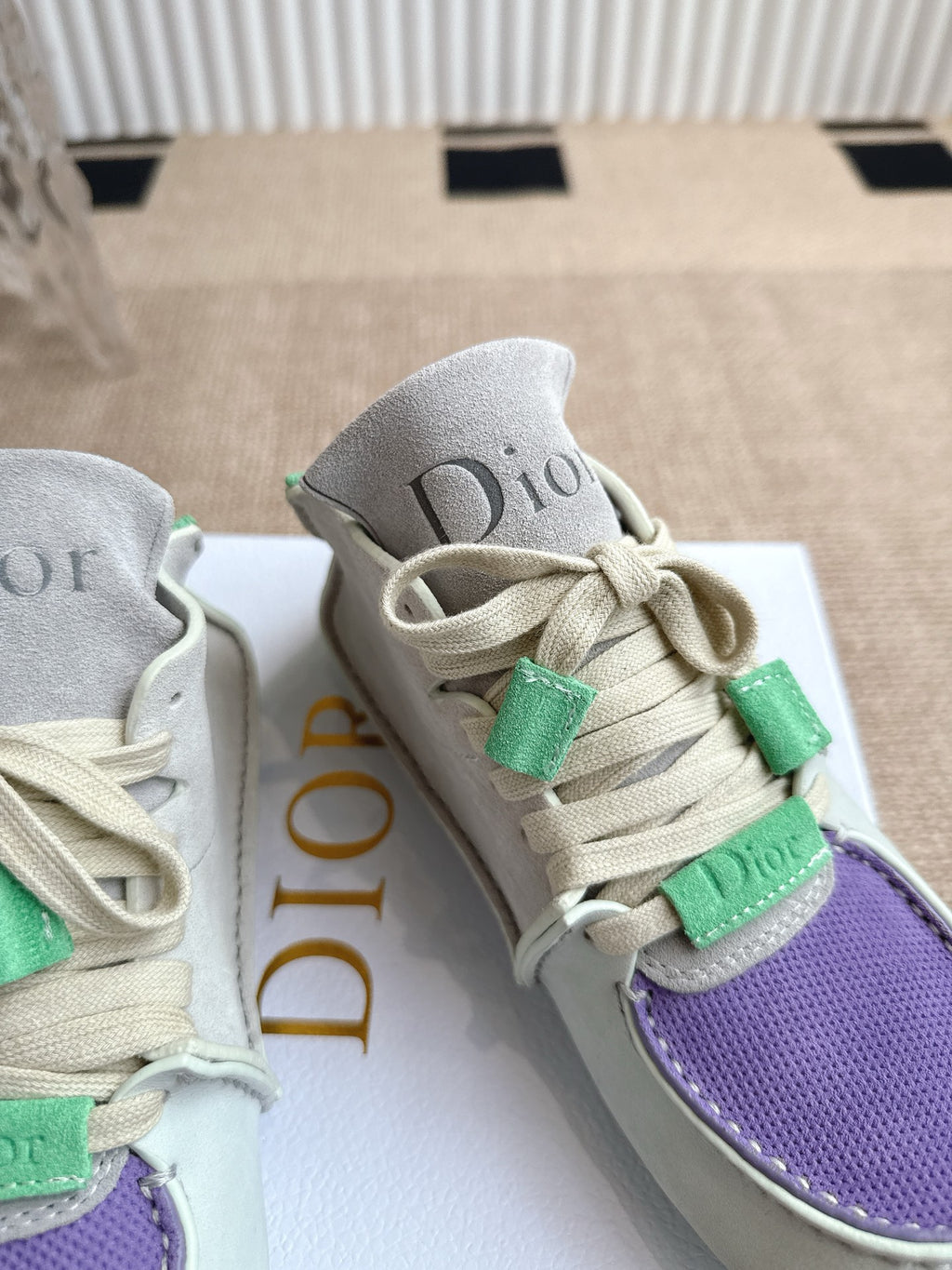 Close-up of light gray Dior sneakers with green lace clips and purple textured toe panel.