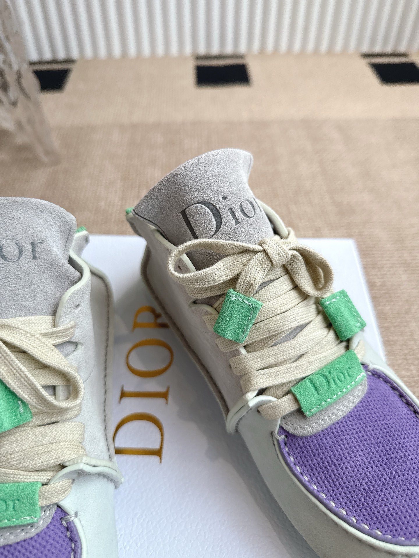 Close-up of light gray Dior sneakers with green lace clips and purple textured toe panel.
