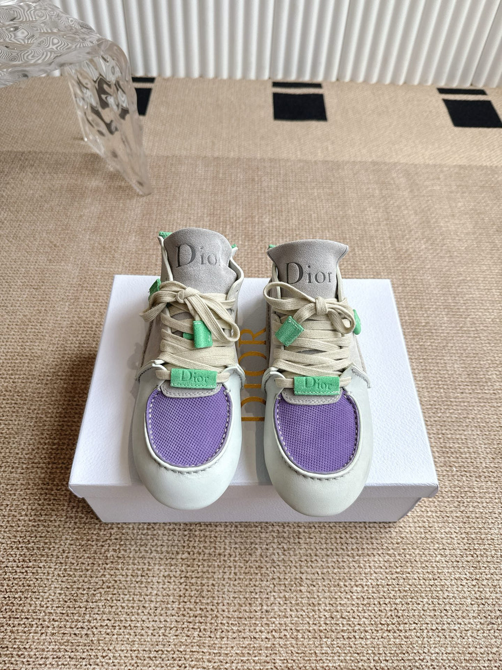 Low-top sneakers on white box: light upper with purple toe and green strap details, Dior.