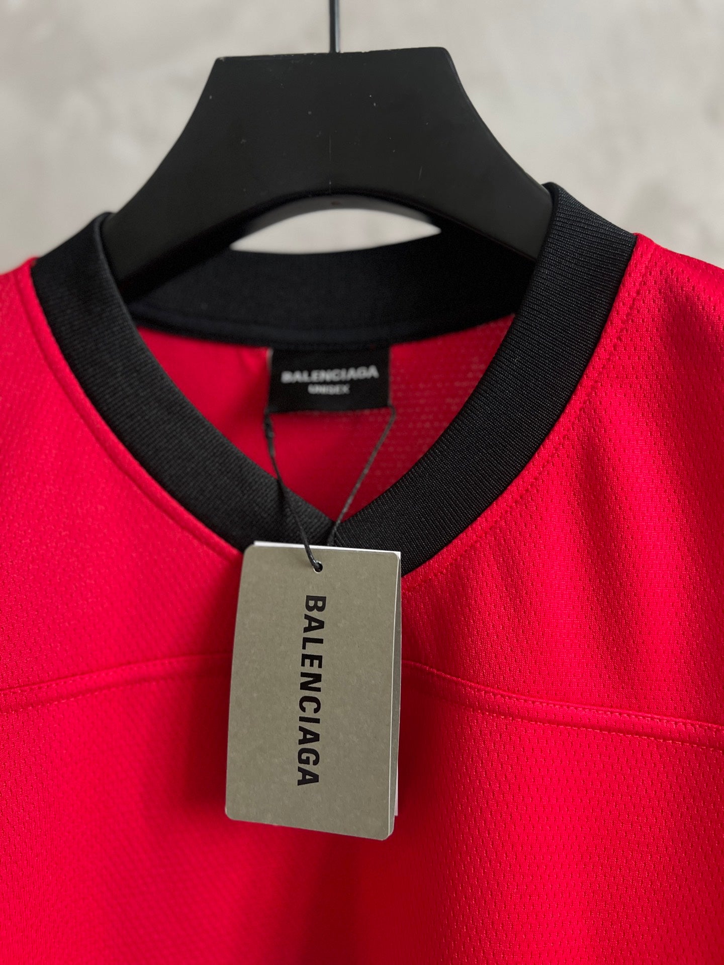 Red short-sleeve jersey on hanger with black V-neck trim and BALENCIAGA hang tag