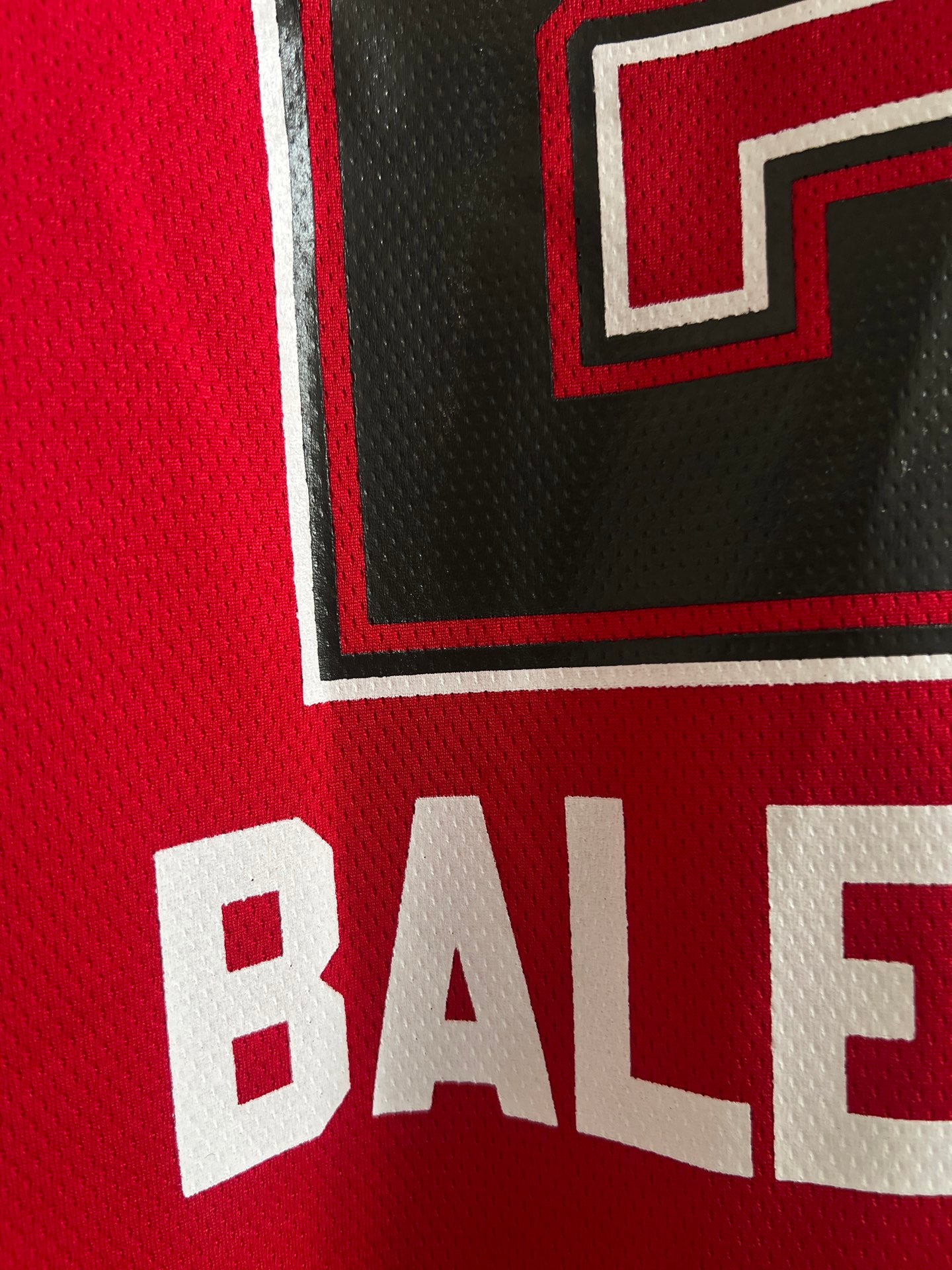 Red jersey fabric close-up of white outlined letter and number graphic on front