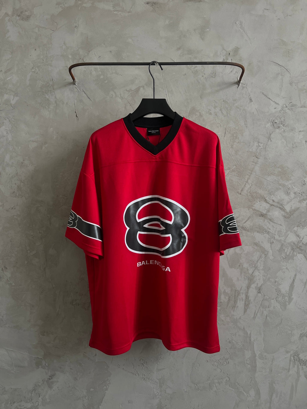 Red short-sleeve jersey with black V-neck trim and large front crest graphic