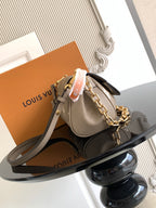 Small designer crossbody bag in gray monogram canvas with gold chain and leather strap.