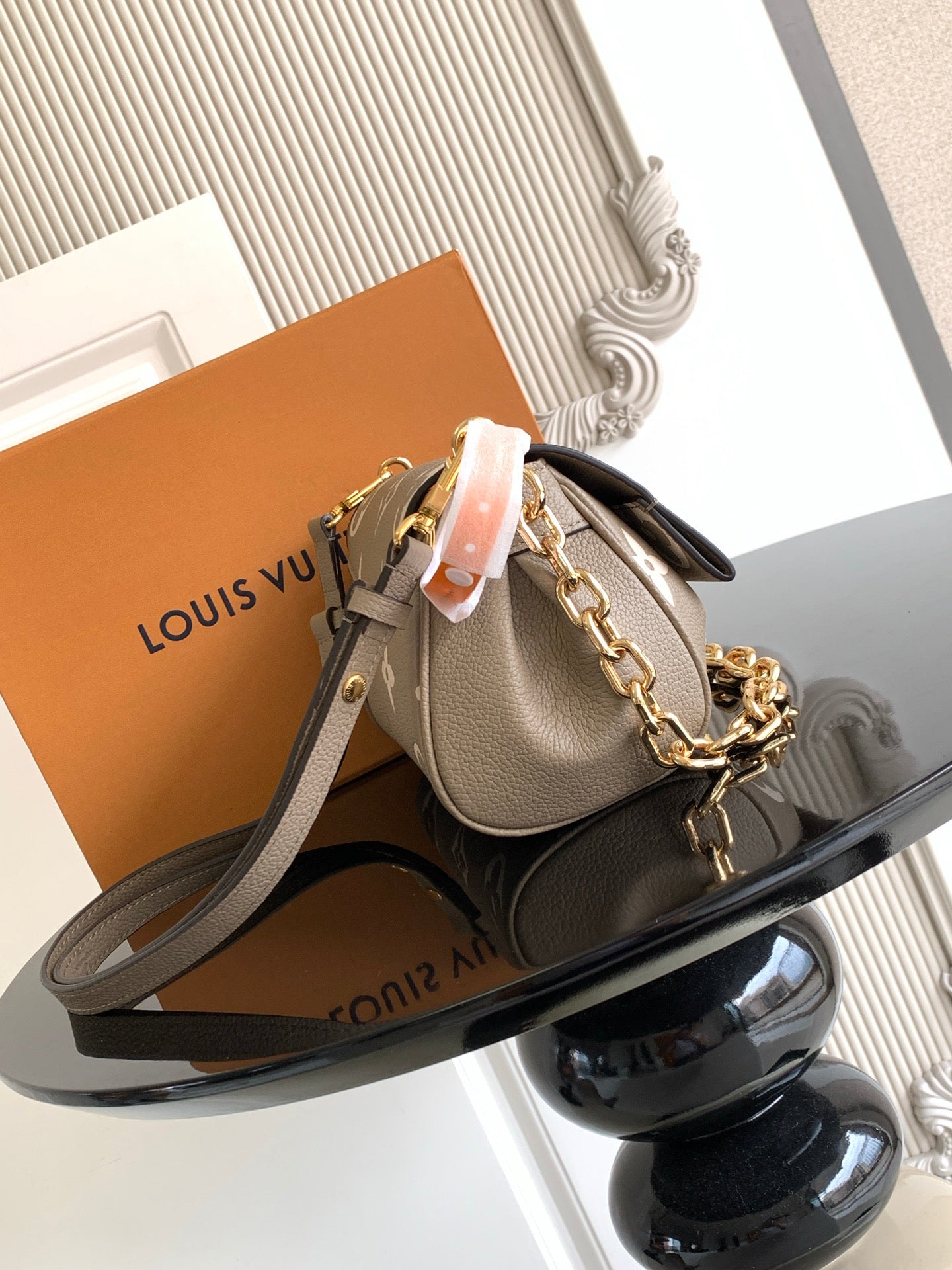 Small designer crossbody bag in gray monogram canvas with gold chain and leather strap.