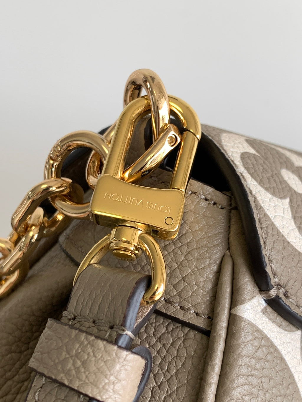 Gray monogram handbag close-up showing gold padlock clasp and chain strap hardware.