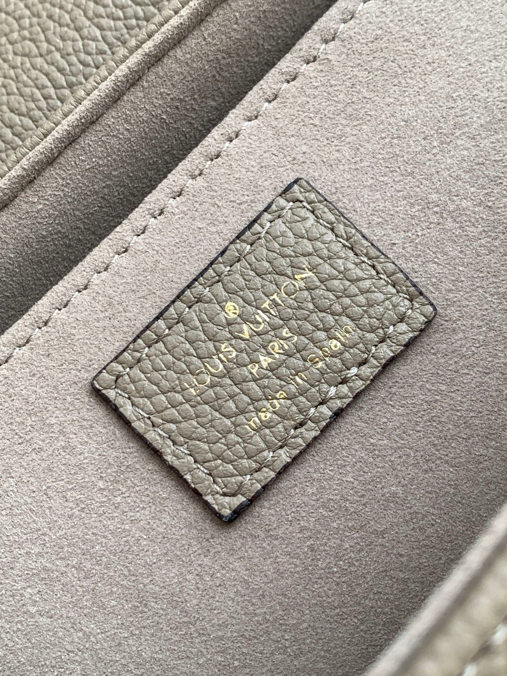 Gray monogram handbag close-up: stitched leather patch with logo on front flap.