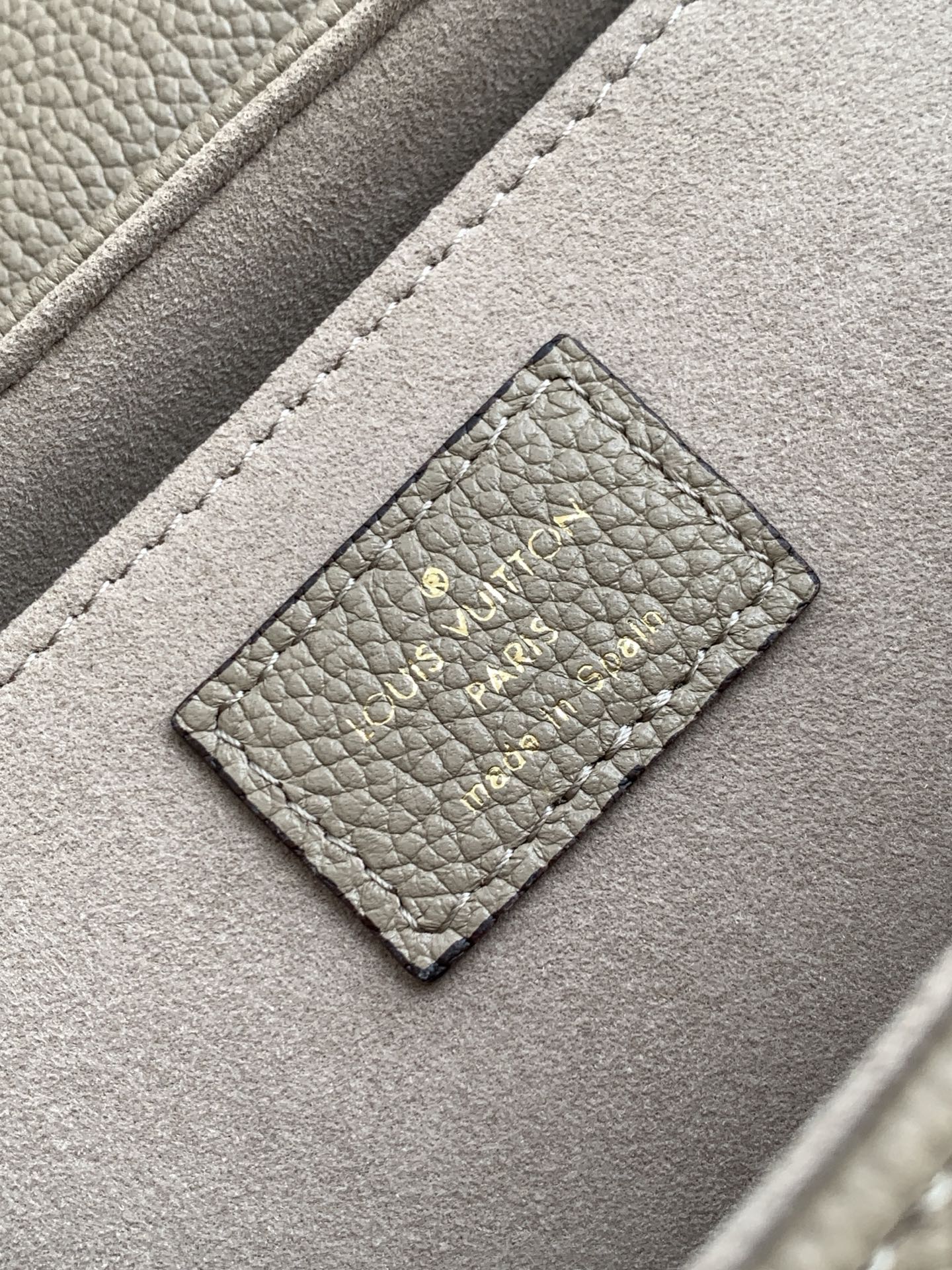 Gray monogram handbag close-up: stitched leather patch with logo on front flap.