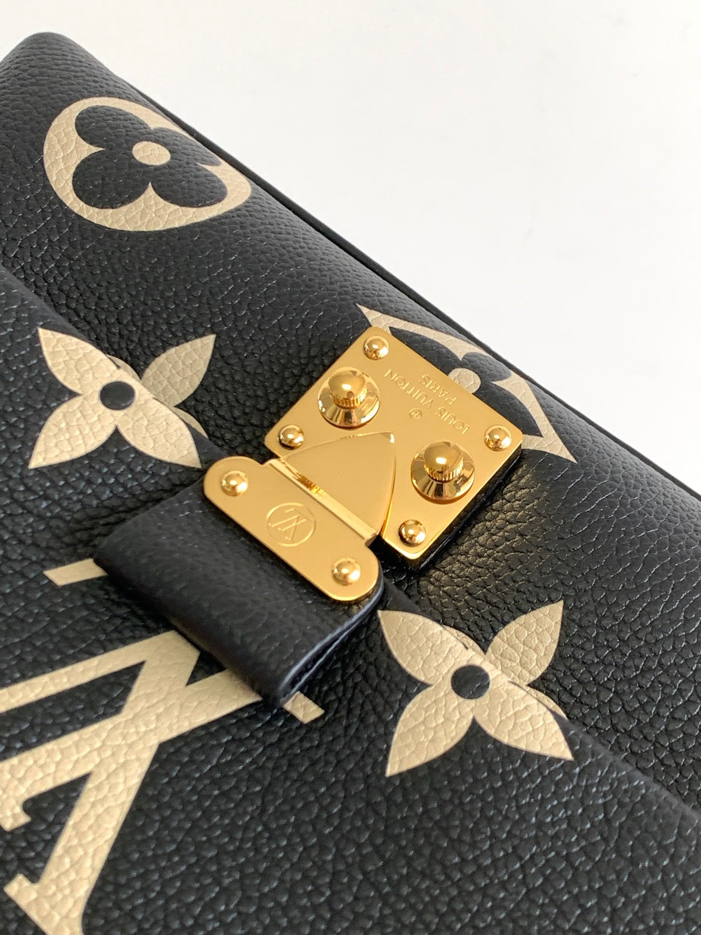 Louis Vuitton monogram bag close-up of gold lockplate and tan floral logos on black