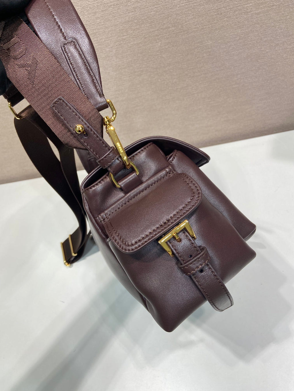 Prada leather bag close-up with front flap, buckle detail, dark brown.