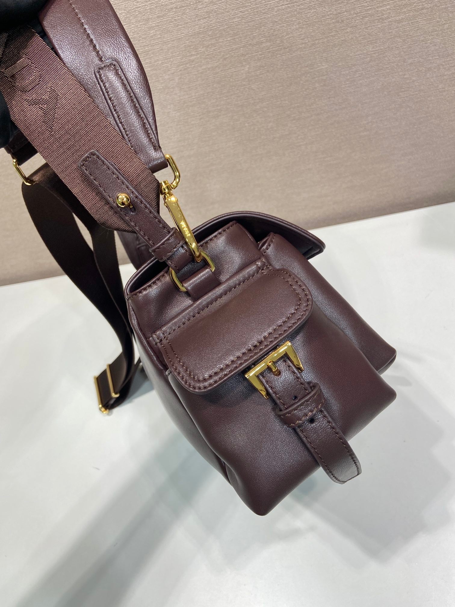 Prada leather bag close-up with front flap, buckle detail, dark brown.