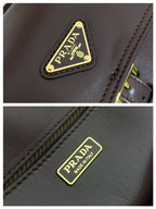 Prada logo patch on dark leather bag with contrast stitching, gold hardware.