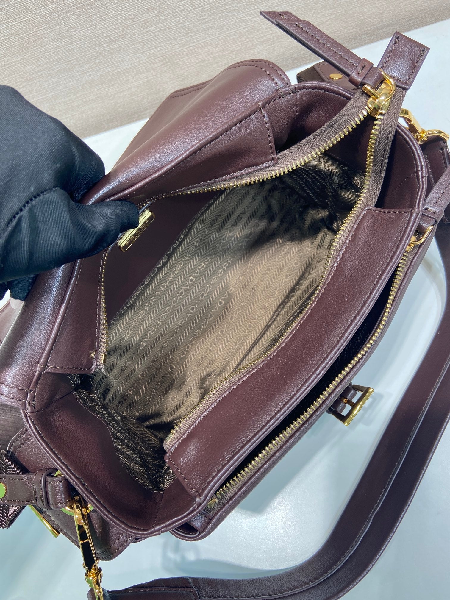Prada leather bag open to show textured fabric lining and gold zipper, dark brown.