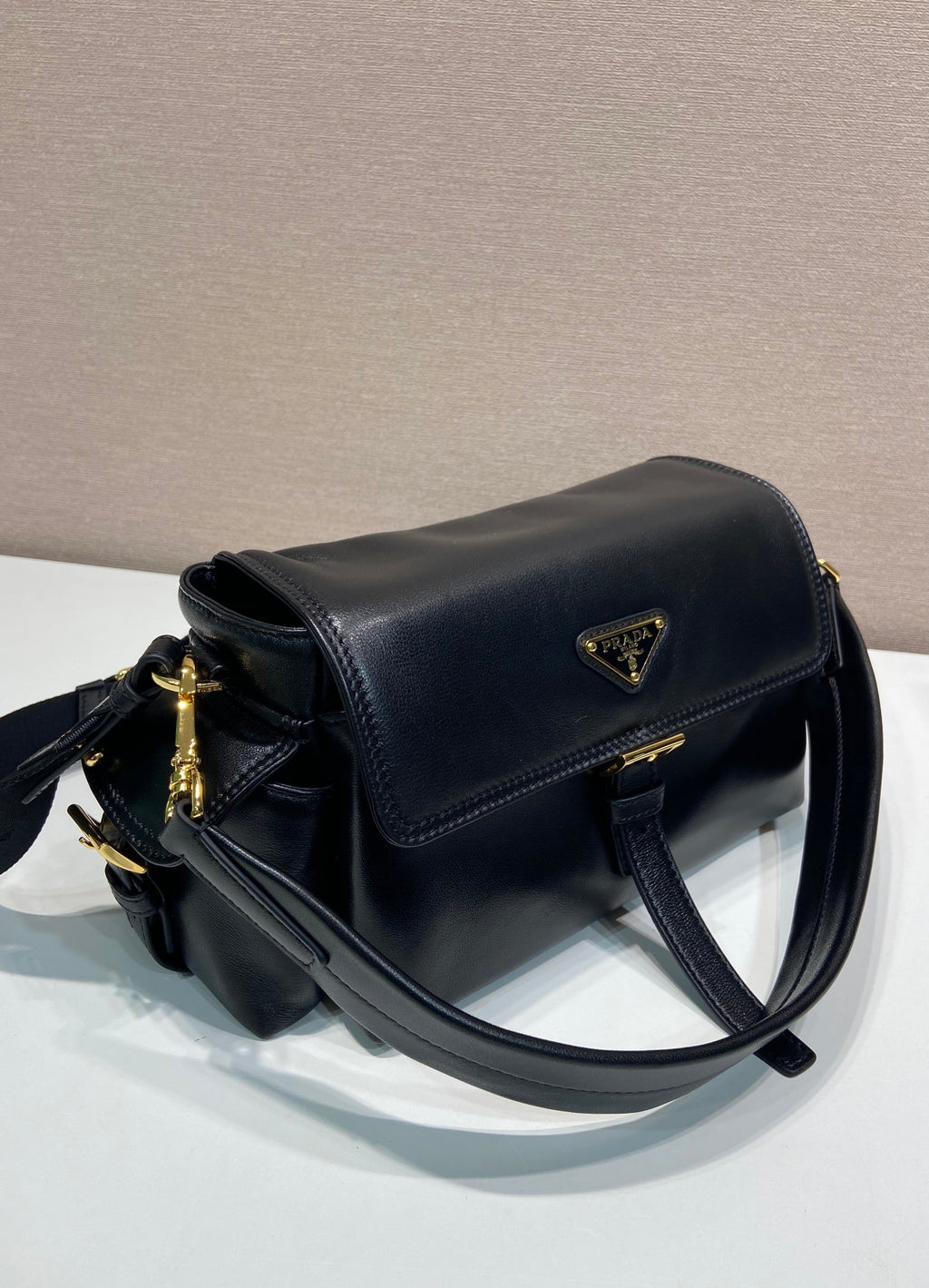 Prada black leather shoulder bag with curved flap, gold zipper pull, and side stitching.